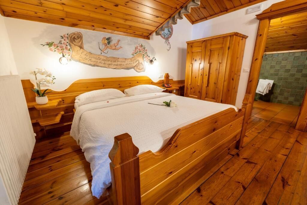 A wooden four-poster bed with a white bedspread, wooden headboard, and footboard, flanked by nightstands with lamps.