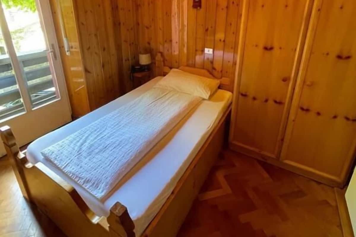 A wooden room with a bed, a nightstand, and a sliding door.
