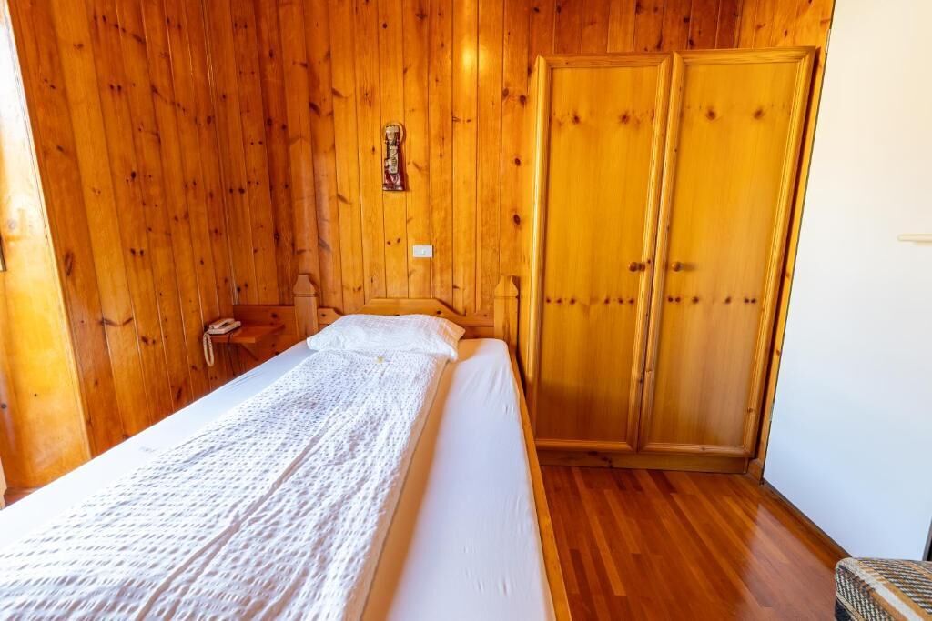 Una habitación de madera con una cama, un armario de madera y una pequeña mesa con una lámpara.