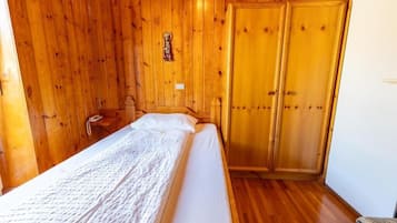 Una habitación de madera con una cama, un armario de madera y una pequeña mesa con una lámpara.
