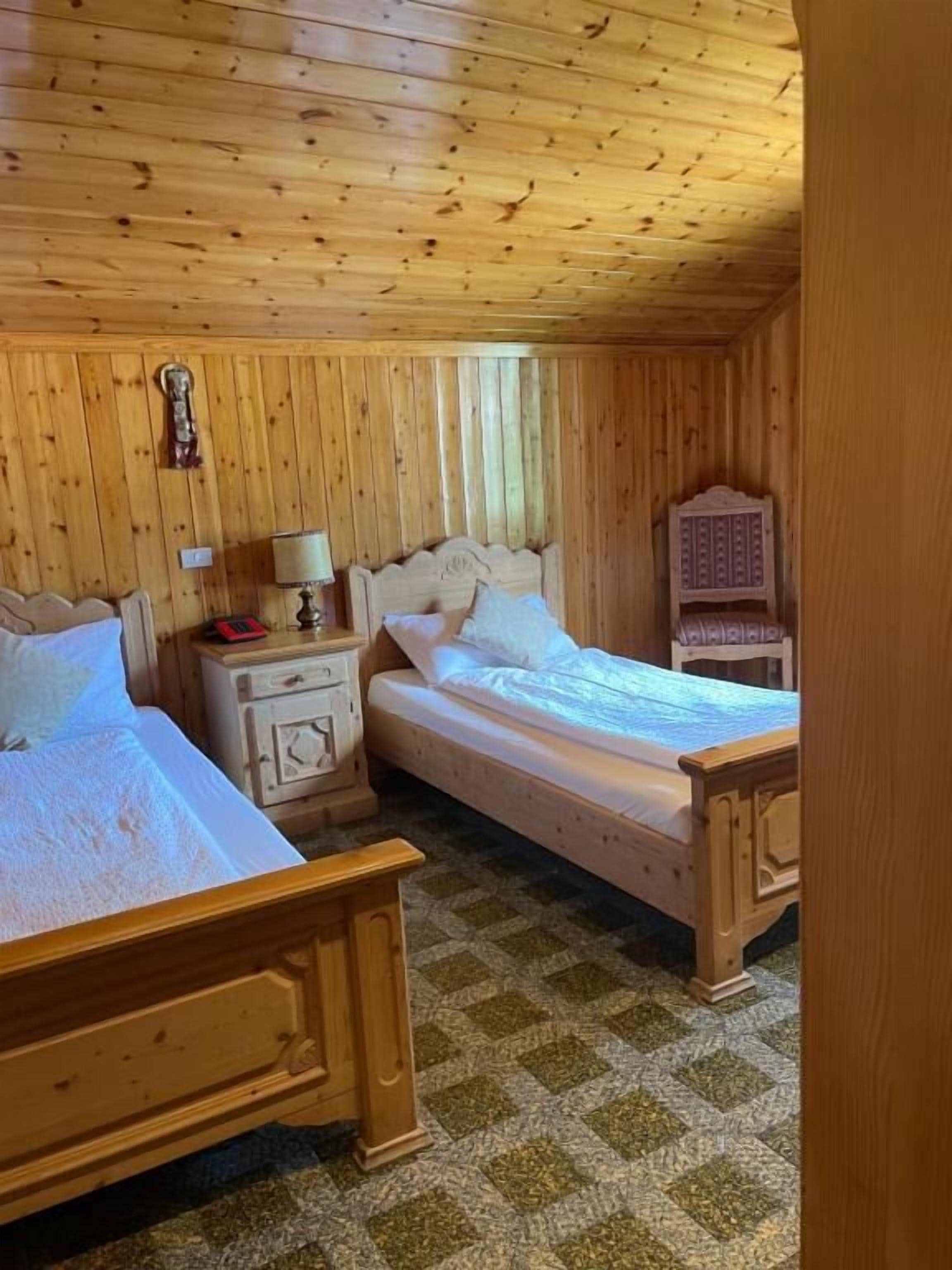 Een houten kamer met twee bedden, een nachtkastje, een lamp en een decoratief object aan de muur.