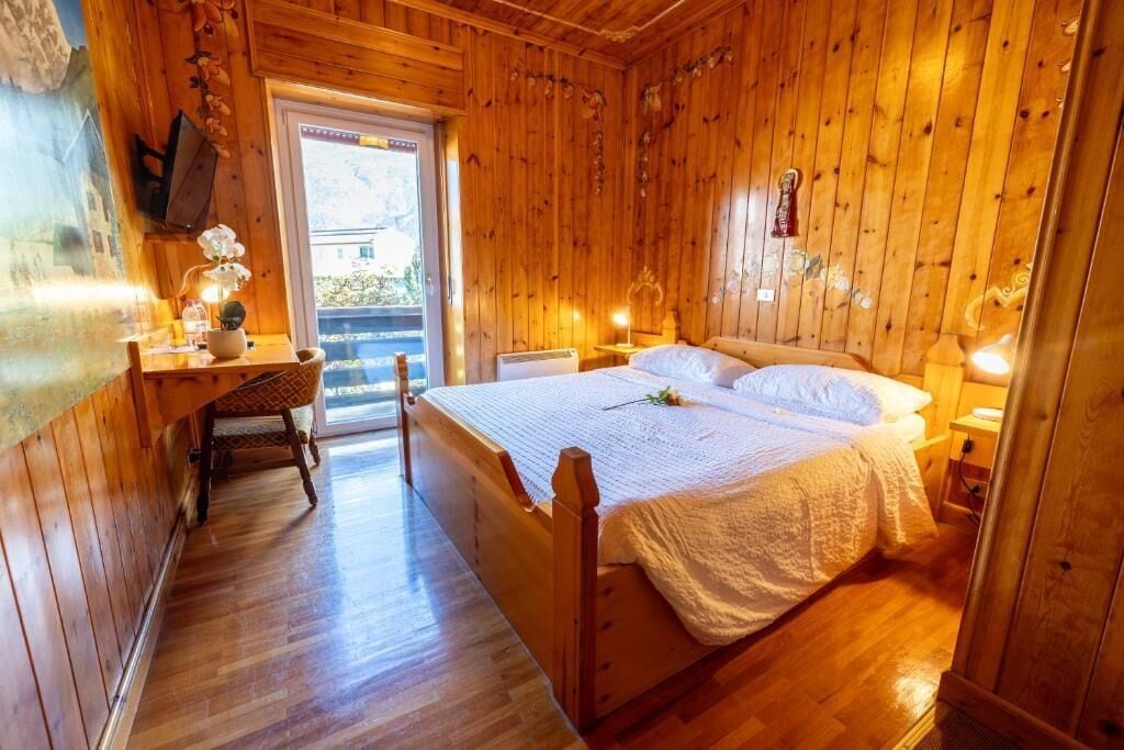 Quarto com painéis de madeira, uma cama, mesas de cabeceira, escrivaninha e uma cadeira.