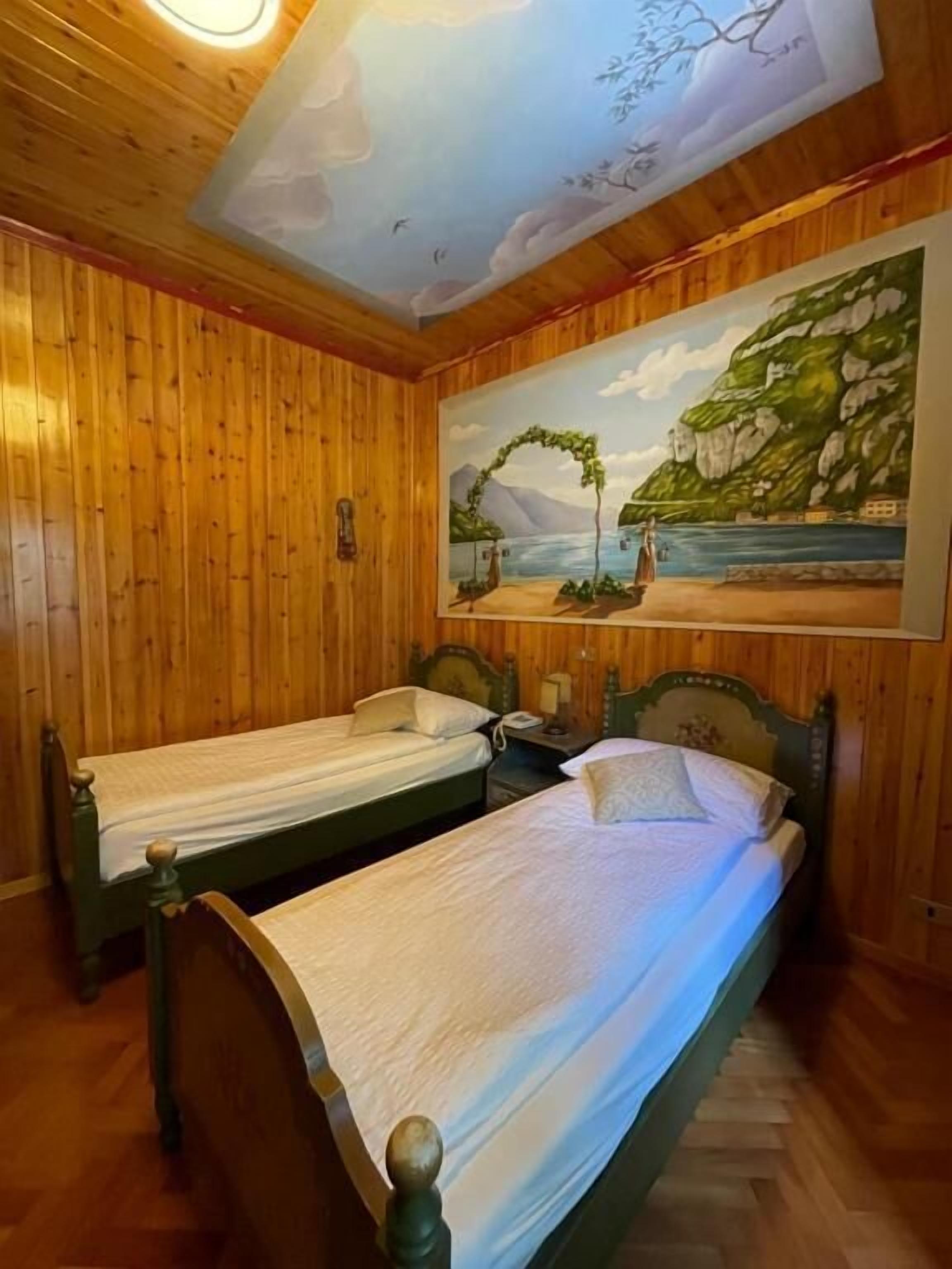 A room with two wooden beds, a painting of a coastal scene, and a wooden ceiling.
