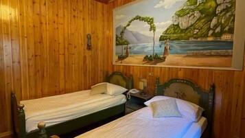 A room with two wooden beds, a painting of a coastal scene, and a wooden ceiling.