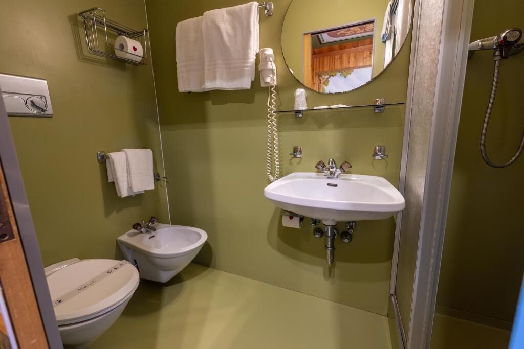 Un baño con inodoro, bidé, lavamanos, perchero para toallas y un espejo.