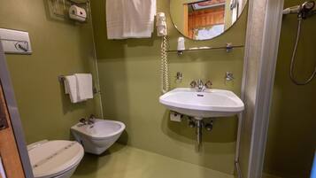 Un baño con inodoro, bidé, lavamanos, perchero para toallas y un espejo.