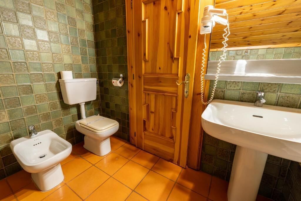 Une salle de bain comprenant des toilettes, un bidet et un lavabo, une porte en bois et des murs carrelés.