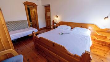 Una cama de madera con colcha blanca, una mesita de noche de madera con lámpara y una silla de madera.