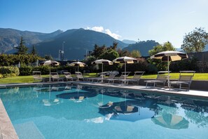 Piscina com cadeiras de sol e guarda-sóis, cercada por vegetação e montanhas ao fundo.