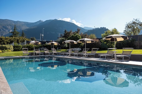 A swimming pool with lounge chairs and umbrellas, surrounded by greenery and mountains in the background.