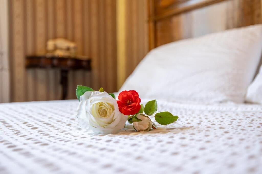 Un letto con una coperta bianca strutturata, una rosa bianca e una rosa rossa.
