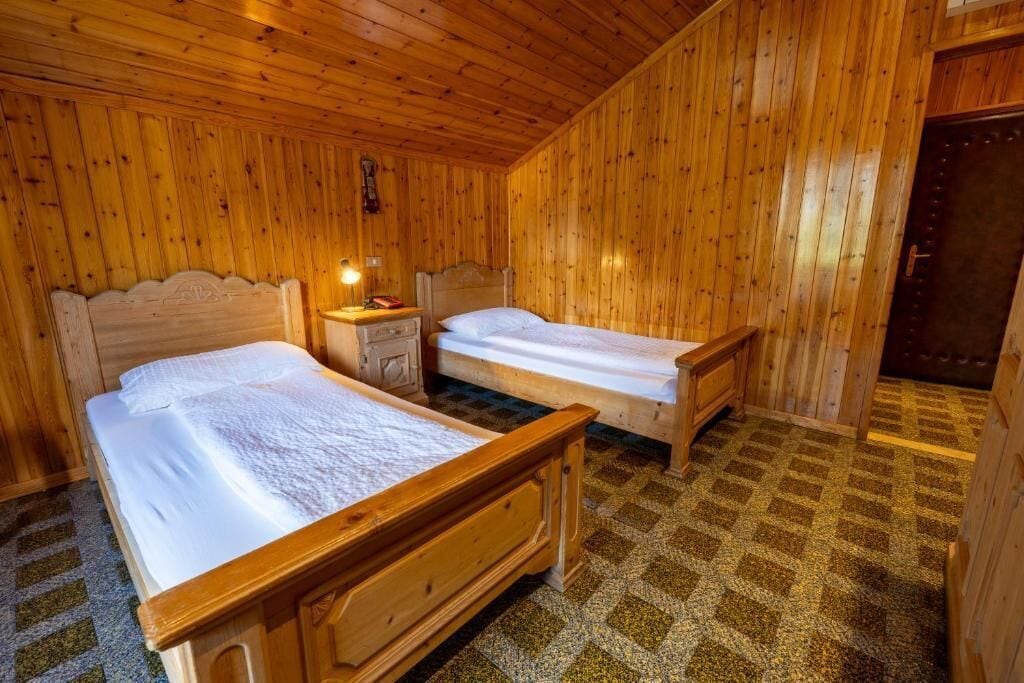 A wooden room with two beds, a nightstand, and a door.