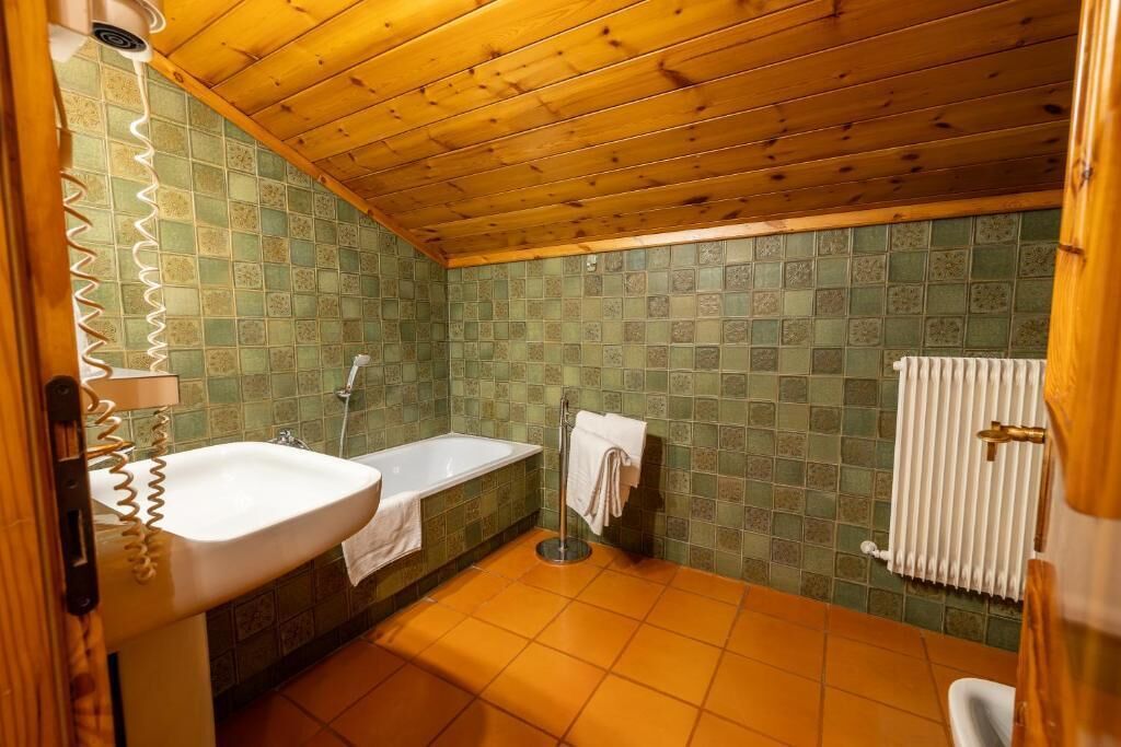 A bathroom with a wooden ceiling, green tiled walls, a white sink, a bathtub, and a toilet.