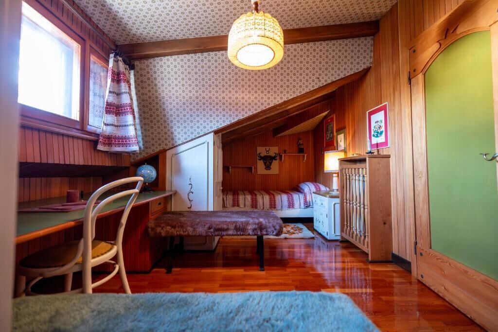 A cozy attic bedroom with a wooden ceiling, a desk, a chair, a bed, and a green door.