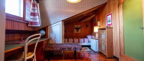 A cozy attic bedroom with a wooden ceiling, a desk, a chair, a bed, and a green door.