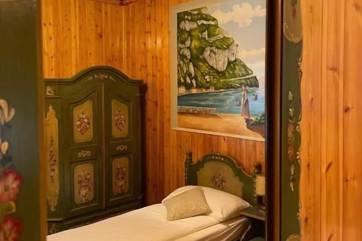 A bedroom with a wooden headboard, a bed with a white mattress, and a painting of a coastal scene on the wall.