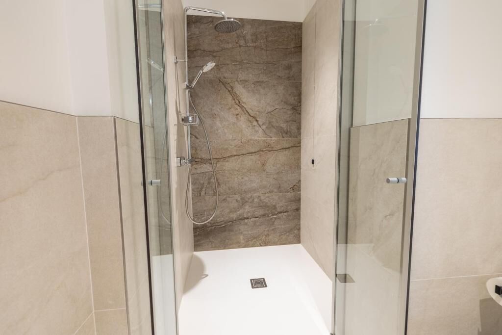 A modern bathroom with a glass-enclosed shower, marble walls, and a white bathtub.