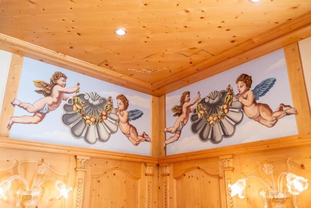 Ein Zimmer mit Holzboden und -wänden, das eine Wandmalerei mit Engeln und Blumen zeigt.