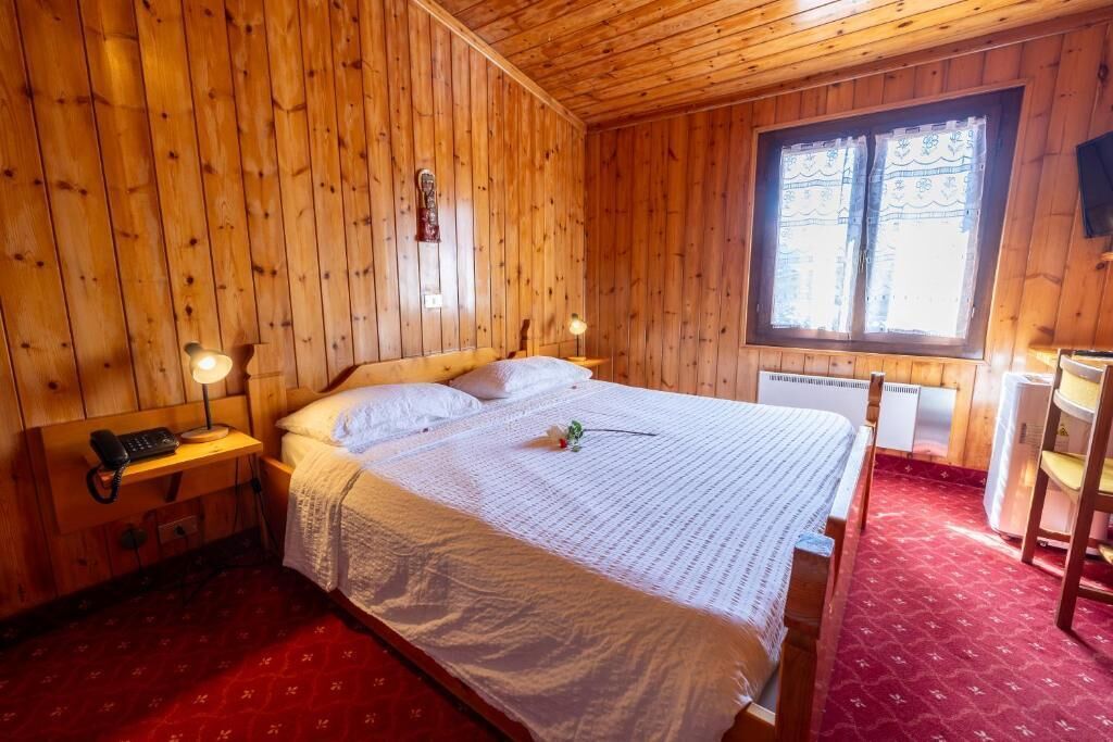 Een kamer met houten lambrisering, een bed, bedlampen, een telefoon en een raam met gordijnen.