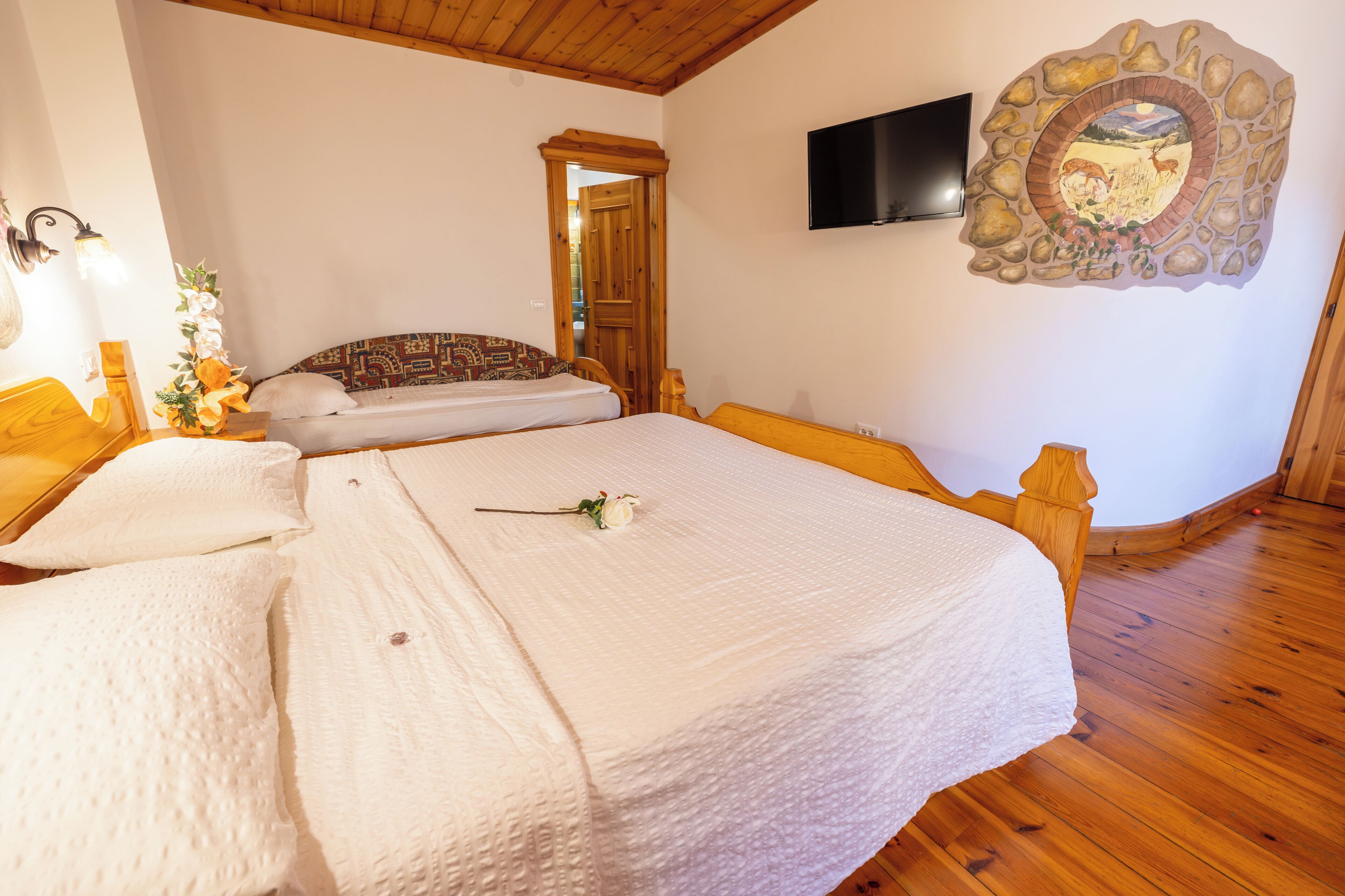 A bedroom with two beds, a wooden floor, a stone wall decoration, and a TV mounted on the wall.