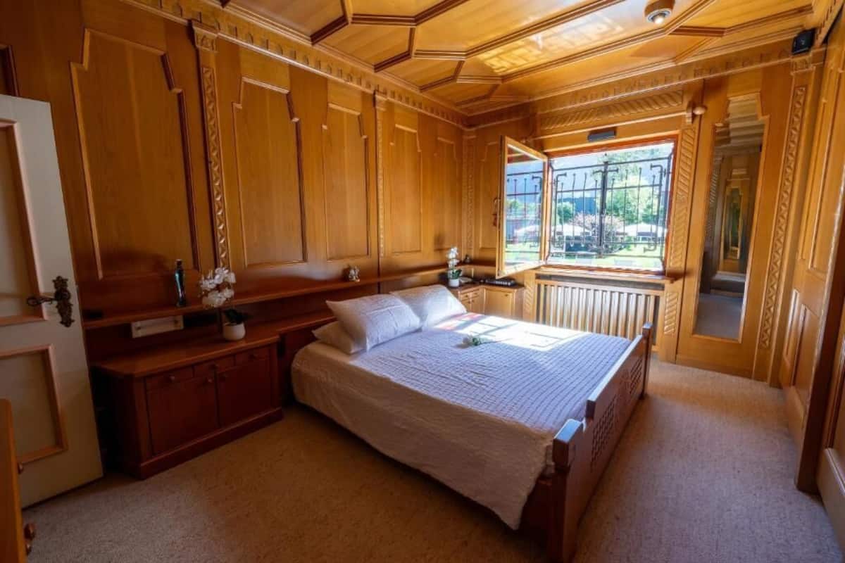A wooden room with a bed, a small table, and a window.