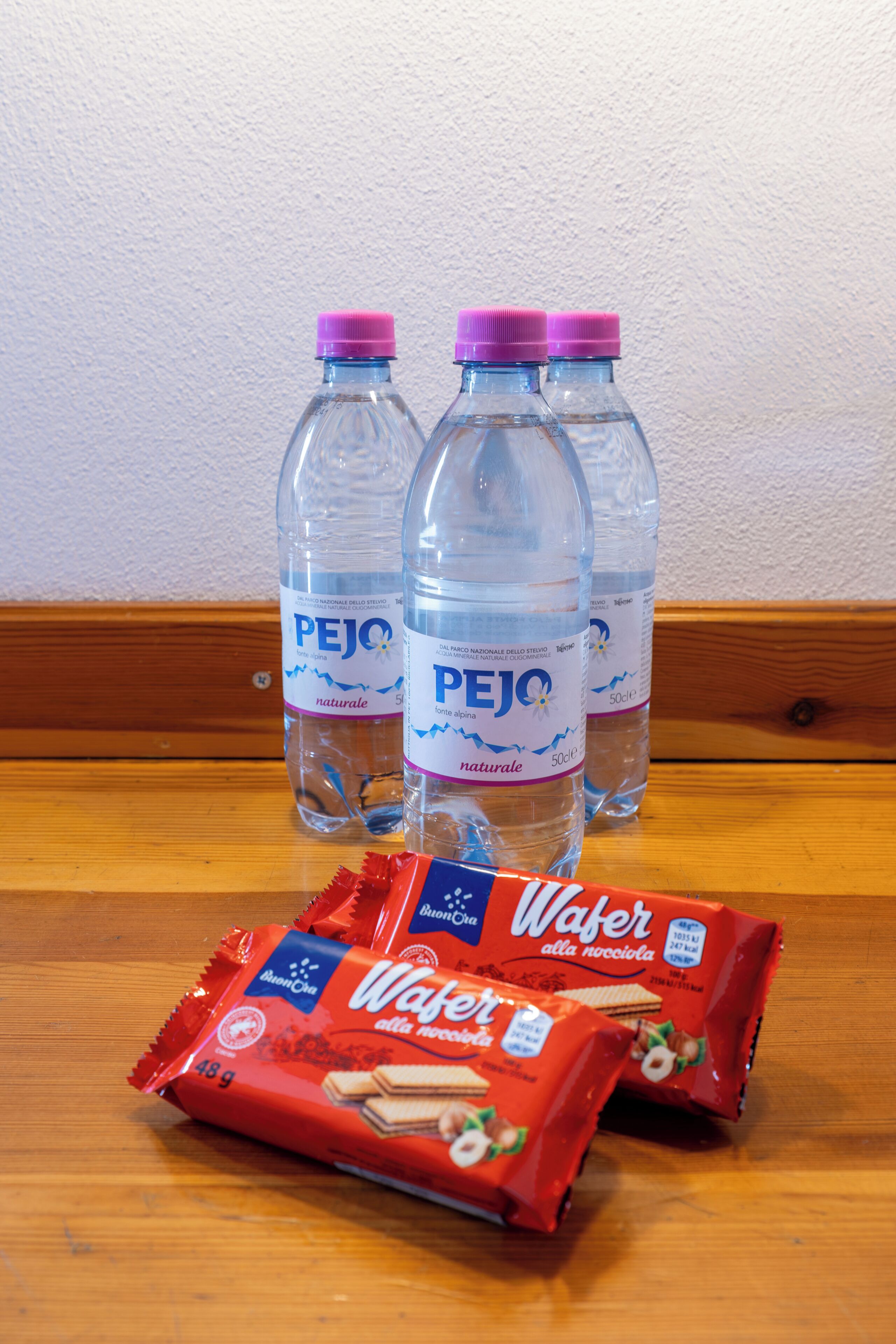 Zwei PEJO-Wasserflaschen und zwei Packungen Wafers auf einer Holzoberfläche.