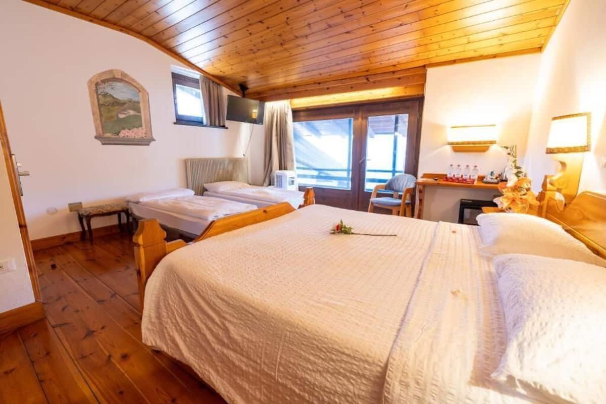 A room with a wooden ceiling, two beds, a bench, a TV, and a window with curtains.