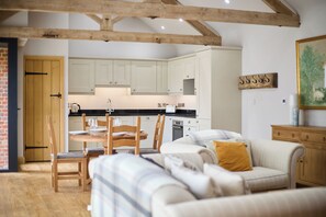 A cozy living area with a sofa, a dining table with chairs, and a kitchen in the background. - The Saddlery (Norwich)