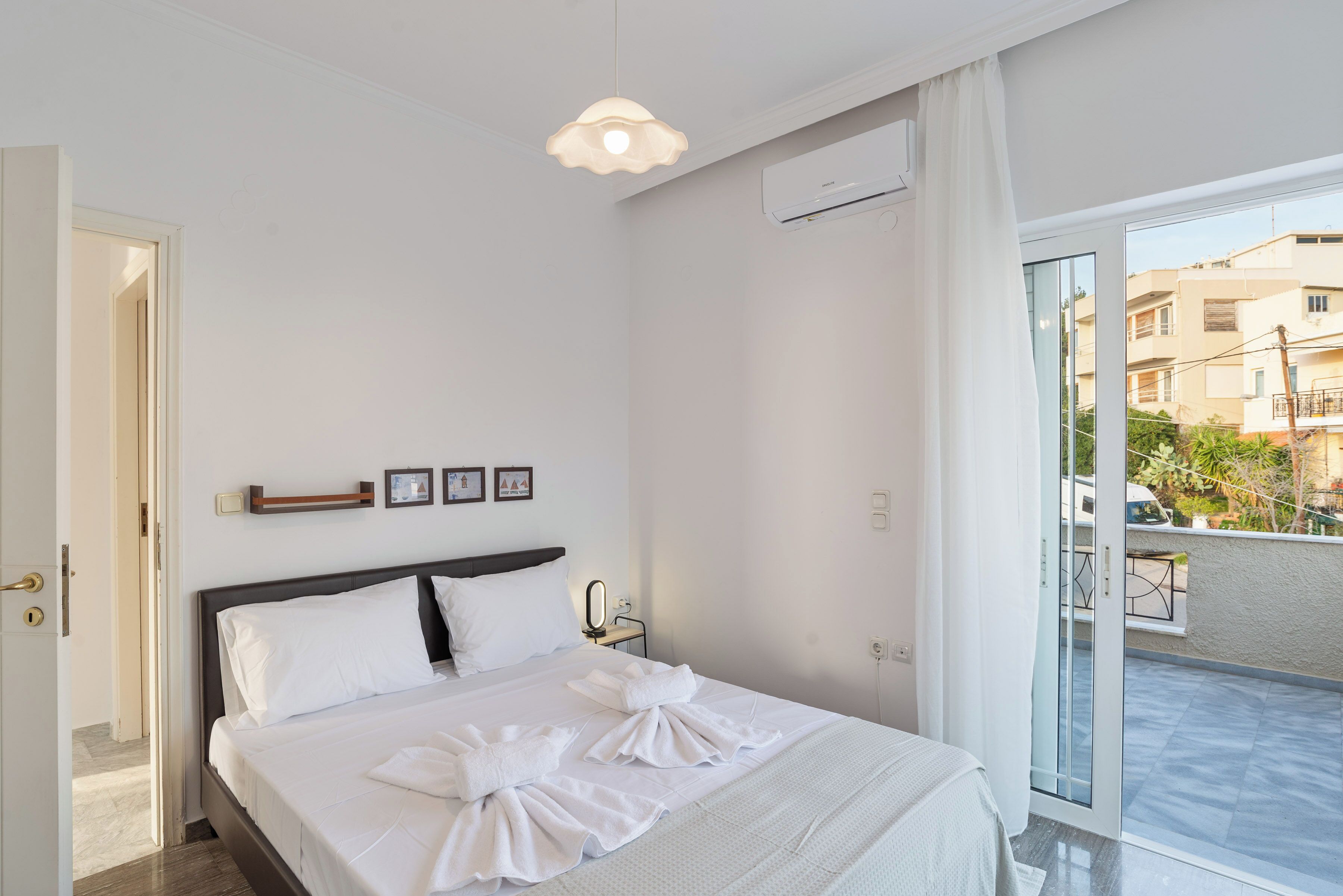 A hotel room with a bed, a bedside table with a mirror, a wall-mounted air conditioner, and a view of the outside balcony.