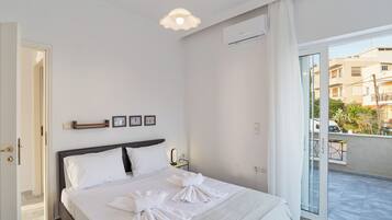 A hotel room with a bed, a bedside table with a mirror, a wall-mounted air conditioner, and a view of the outside balcony.