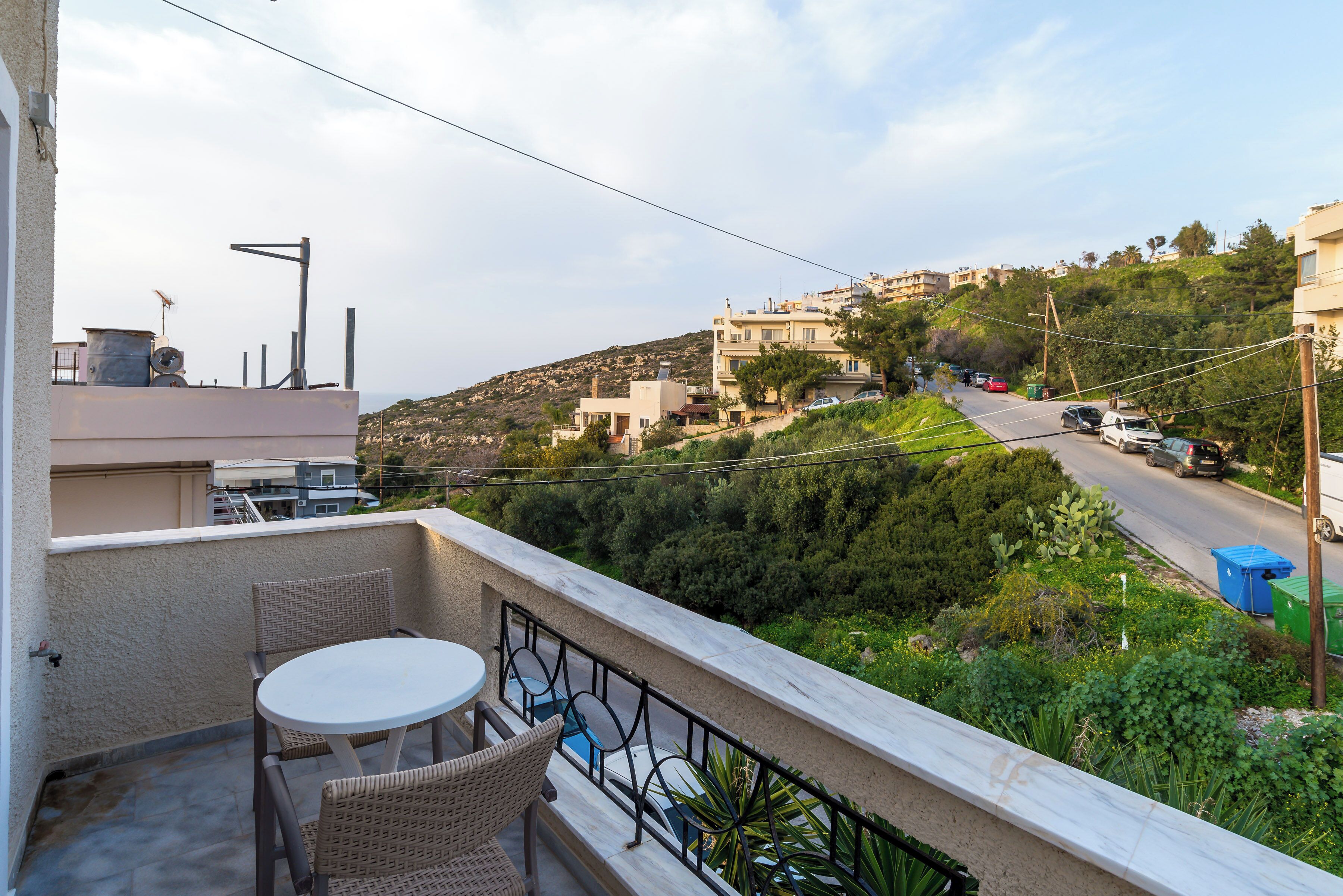 A balcony with wicker furniture, a view of a road, and buildings in the distance.