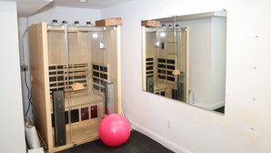 Une pièce équipée d’un sauna, d’un grand miroir et d’un ballon d’exercice rose.