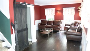 Un salon avec un ensemble de canapés en cuir marron, une table basse en verre et une porte en bois foncé.