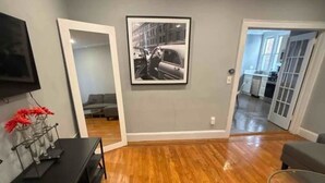 A living room with hardwood flooring, a black entertainment unit, a framed picture on the wall, and a doorway leading to another room.
