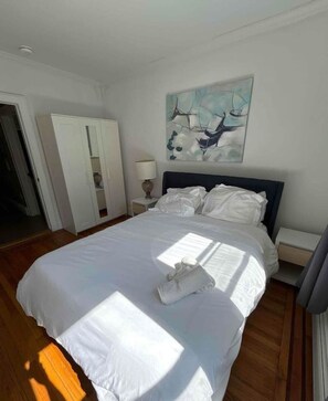 A bedroom with a bed, a nightstand, a lamp, a wardrobe, and a painting on the wall. - Beautiful 2BR/1BA Apt close to NYC! (Jersey City)