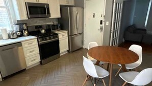 A modern kitchen with white cabinets, stainless steel appliances, and a herringbone wood floor.