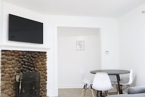 Una habitación con chimenea de piedra, un televisor de pantalla plana montado encima, una mesa redonda de comedor con sillas blancas y un cuadro en la pared.