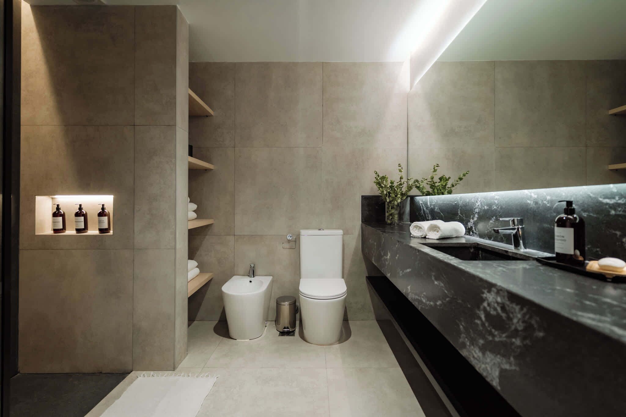 Ein modernes Badezimmer mit Marmorplatte, einem Bidet, einer Toilette und einem Ablagefach mit Pflegeprodukten.