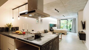 A modern kitchen with a central island, a dining area with a sofa, and a bedroom with a large window. - Portal Arévalo in Palermo by Magno | 21 (Buenos Aires)