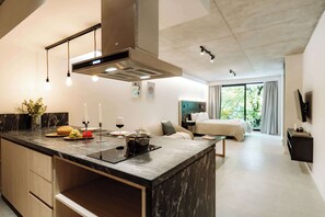 A modern kitchen with a central island, a dining area with a sofa, and a bedroom with a large window. - Portal Arévalo in Palermo by Magno | 21 (Buenos Aires)
