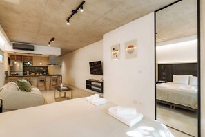 A modern hotel room with a bed, a small seating area, a kitchenette, and a large mirror. - Portal Arevalo in Palermo by Magno | 32 (Buenos Aires)