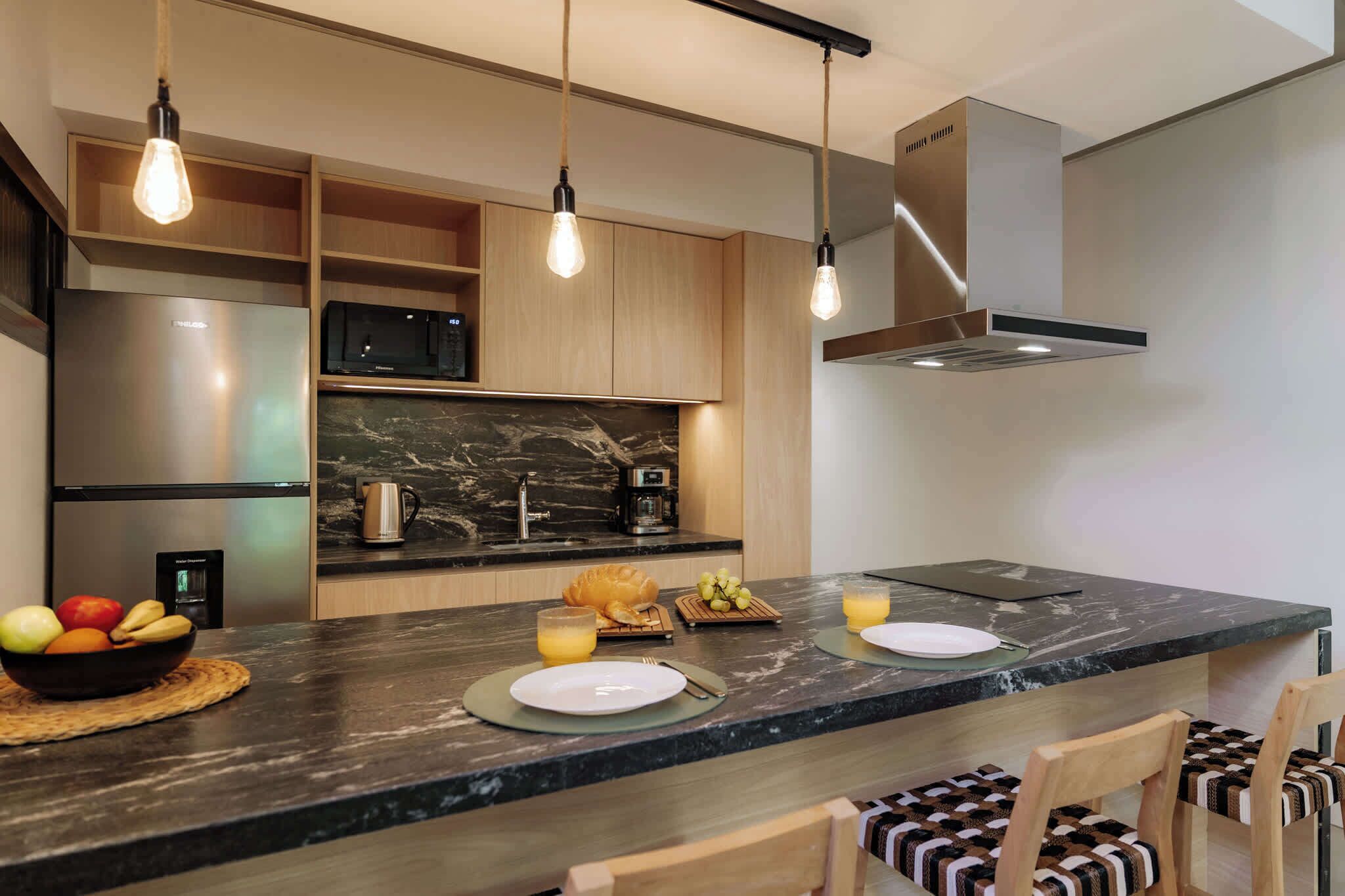 Une cuisine moderne dotée d’un plan de travail en marbre, d’appareils électroménagers en acier inoxydable, d’armoires en bois et de luminaires suspendus.