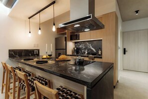 Eine moderne Küche mit einer zentralen Kochinsel, Pendelleuchten, einer Edelstahl-Dunstabzugshaube und Holzstühlen.