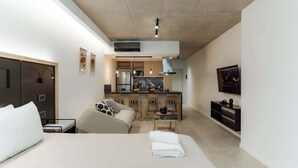 A modern hotel room with a bed, a sofa, a small kitchen area, and a TV. - Portal Arévalo in Palermo by Magno | 12 (Buenos Aires)