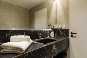 Ein modernes Badezimmer mit einem schwarzen Marmorwaschbecken, einem Handtuch, einem Spiegel und einer Topfpflanze.