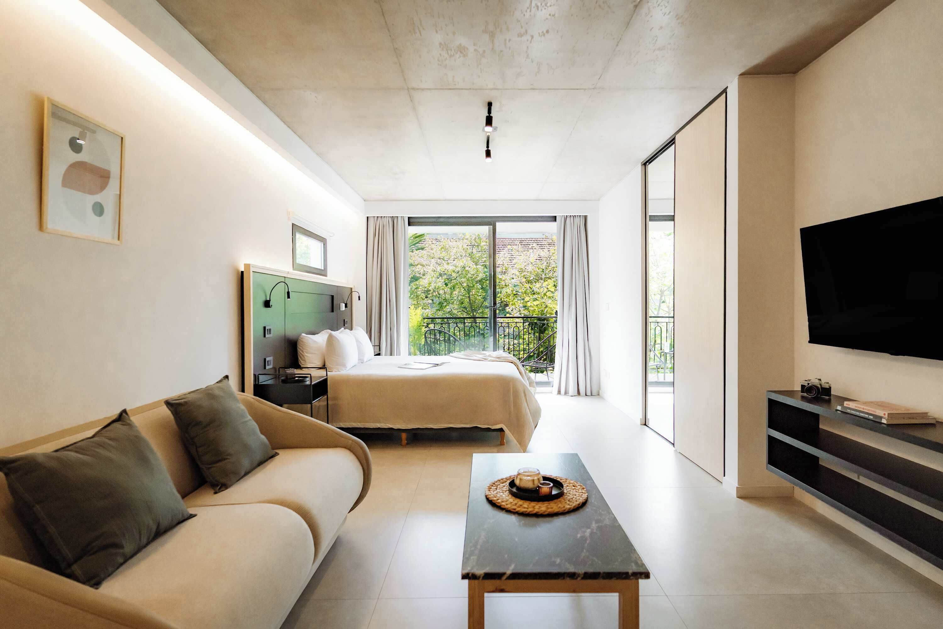 Una habitación de hotel moderna con cama, sofá, mesa de centro, televisor y balcón con vistas.