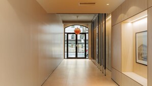 A modern hallway with a glass door leading to a street view, a hanging light fixture, and a framed picture on the wall. - Portal Arévalo in Palermo by Magno | 41 (Buenos Aires)