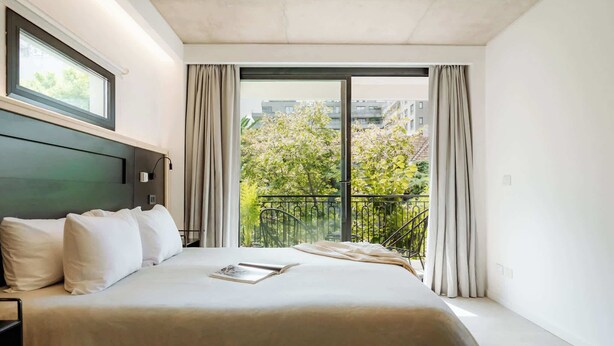 A modern hotel room with a large bed, a view of the outdoors, and a balcony with a railing. - Portal Arévalo in Palermo by Magno | 41 (Buenos Aires)