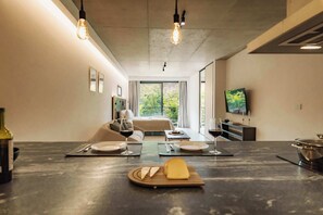Eine moderne Küche mit Marmorarbeitsplatte, eine Essecke mit Tisch für zwei Personen und ein Schlafzimmer mit Bett und Fernseher.