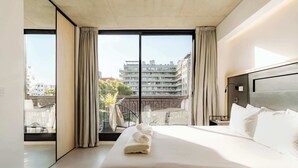Ett modernt hotellrum med en stor säng, utsikt över staden och en balkong med gardiner.